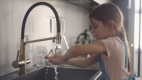 Händewaschen-In-Der-Küche,-Kleines-Mädchen-In-Schürze-Reibt-Ihre-Handflächen-Unter-Dem-Wasserstrahl-Aus-Dem-Wasserhahn
